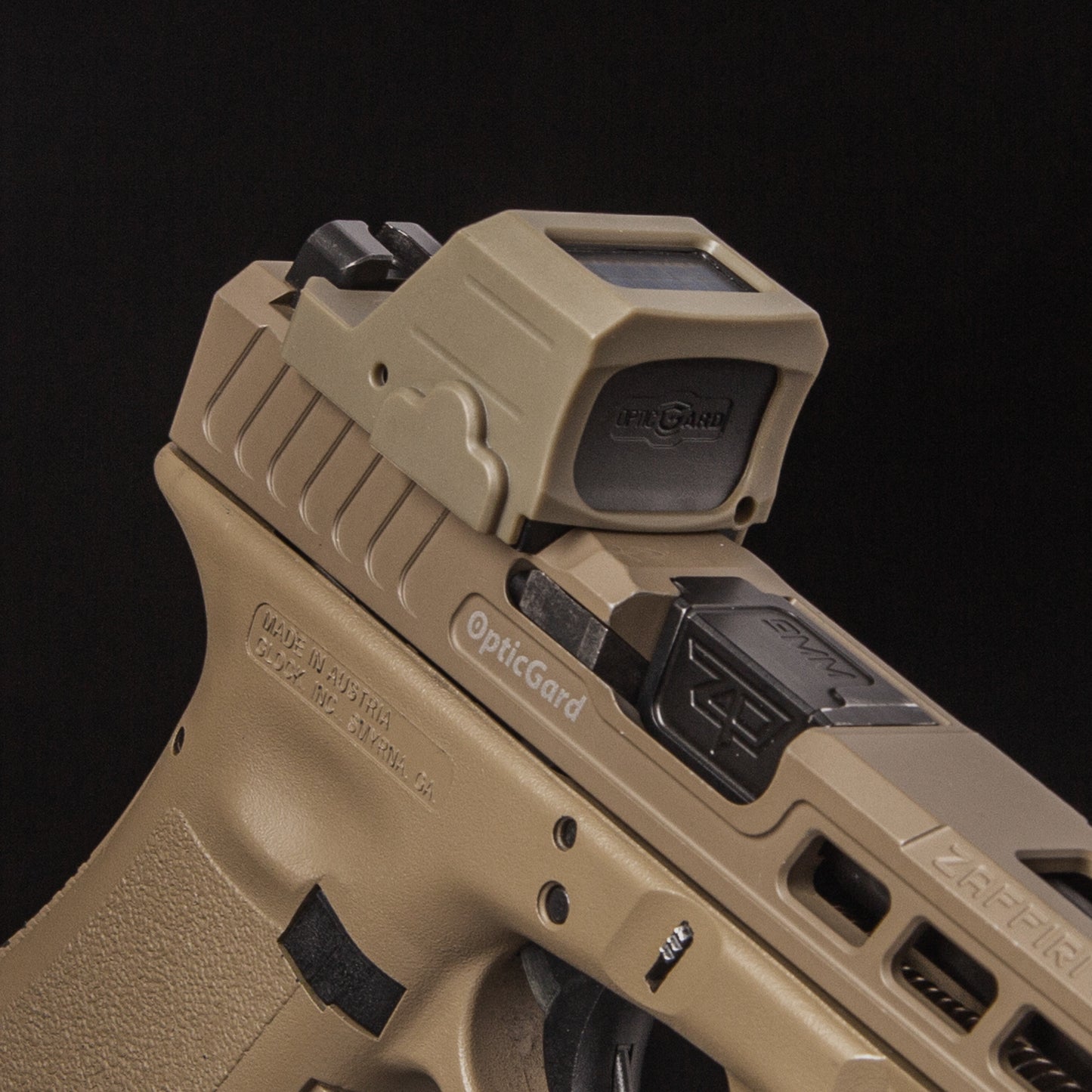 A close-up of a tan OpticGard cover for holosun 507CX3 mounted on a tan handgun against a solid black background. [ads-hide]