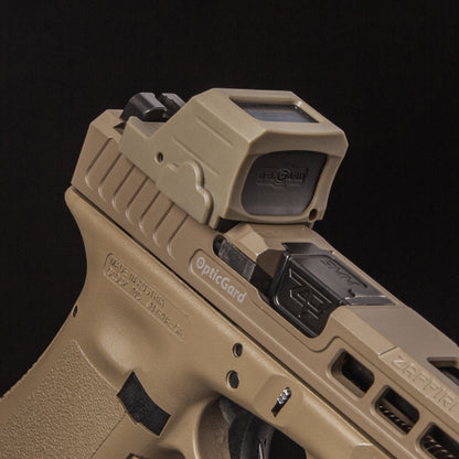 A close-up of a tan OpticGard cover for holosun 507CX3 mounted on a tan handgun against a solid black background. [ads-hide]