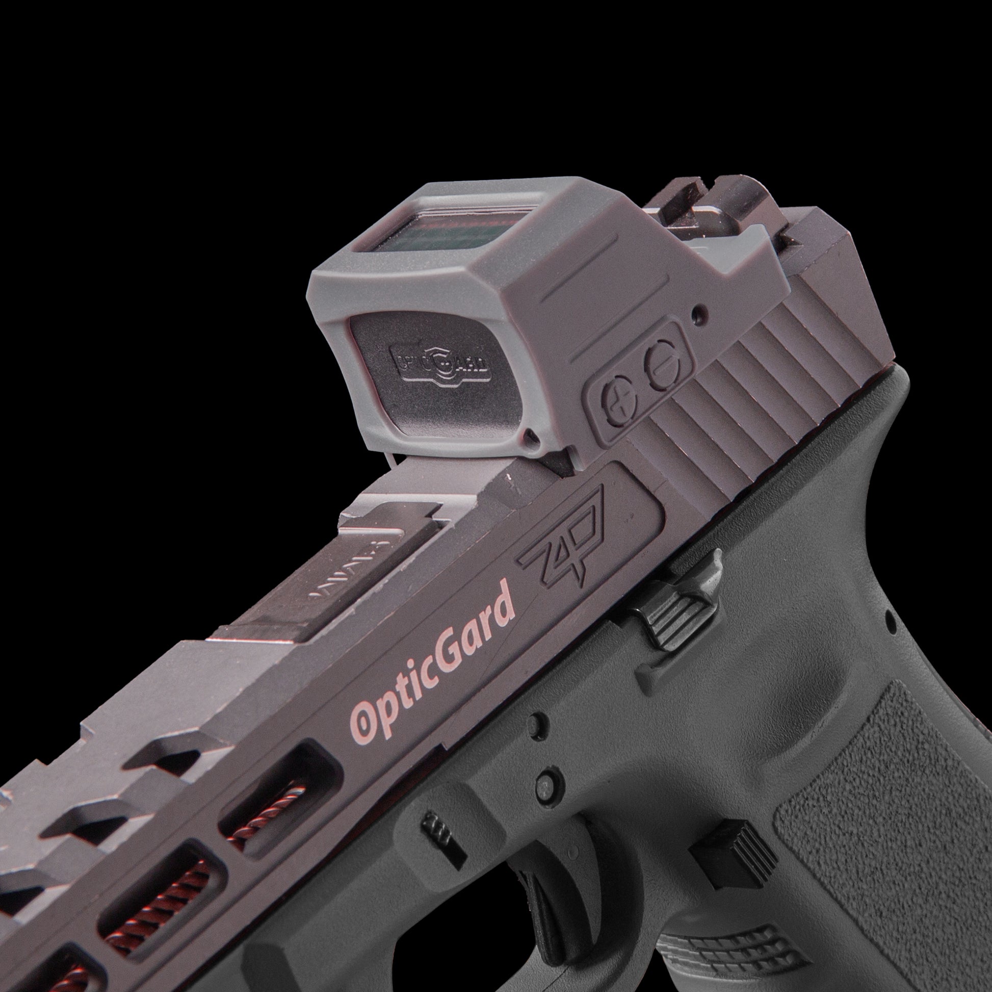 A close-up studio shot of a handgun with a mounted Gray OpticGard red dot Cover for Holosun 507CX3 against a solid black background. [ads-hide]