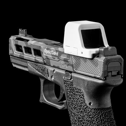 A semi-automatic handgun with a camouflage pattern slide, a white Opticgard Cover installed, shown against a solid black background. [ads-hide]