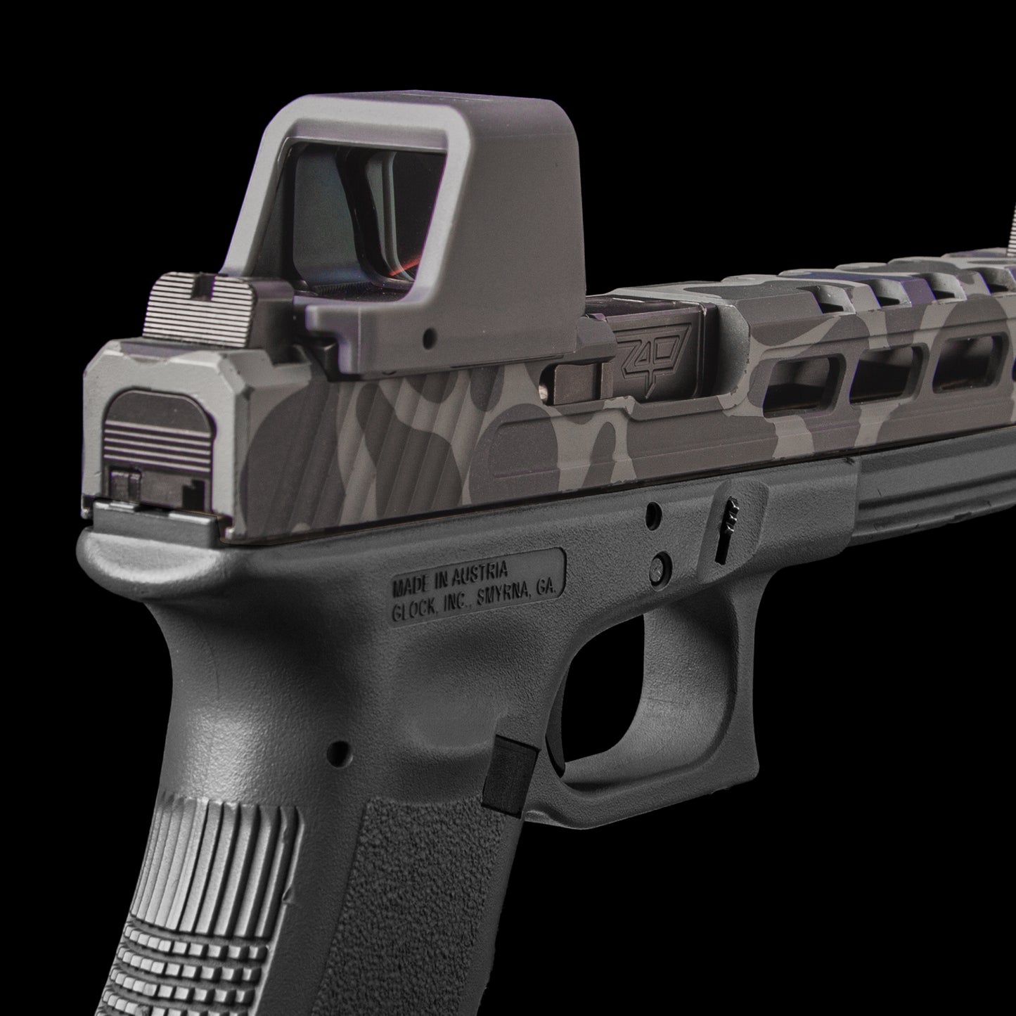 A close-up studio shot of a semi-automatic handgun with a gray and black camouflage pattern on the slide, featuring a gray opticgard cover set against a solid black background. [ads-hide]